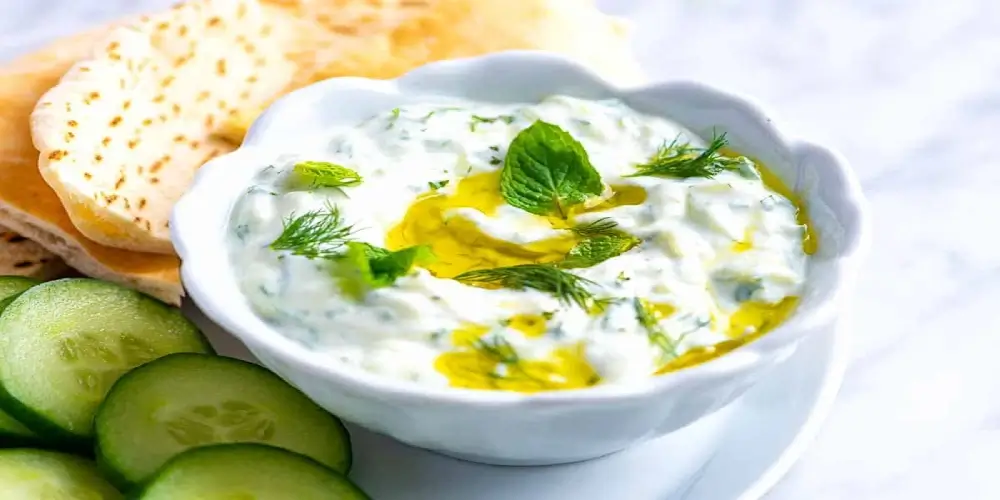 A white bowl filled with creamy tzatziki, garnished with fresh herbs and a drizzle of olive oil.