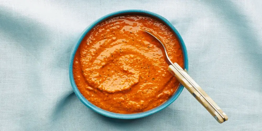 A blue bowl filled with a vibrant red romesco sauce.